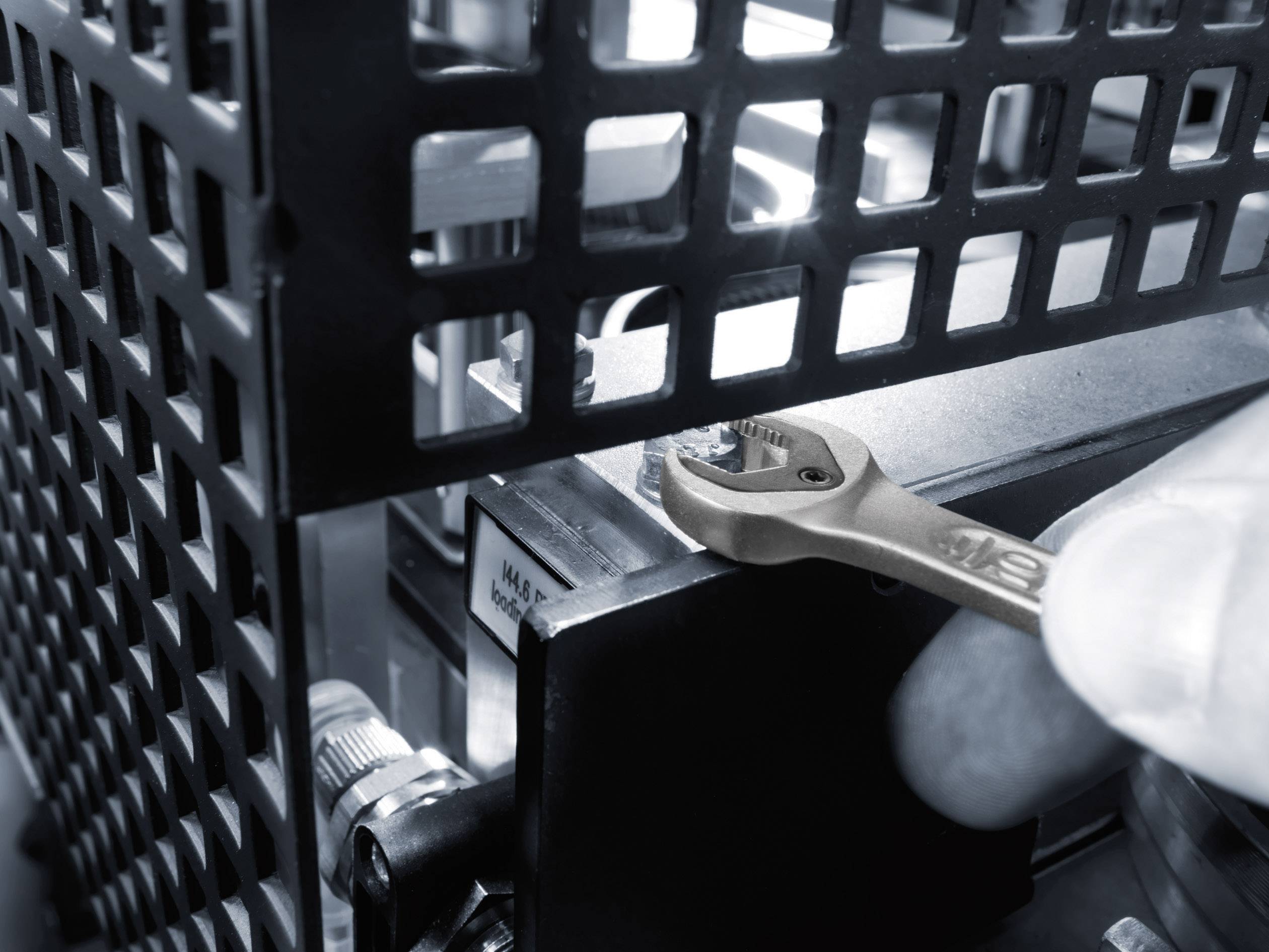 A hand holds a spanner and tightens a nut in a mechanical structure. The environment appears industrial.