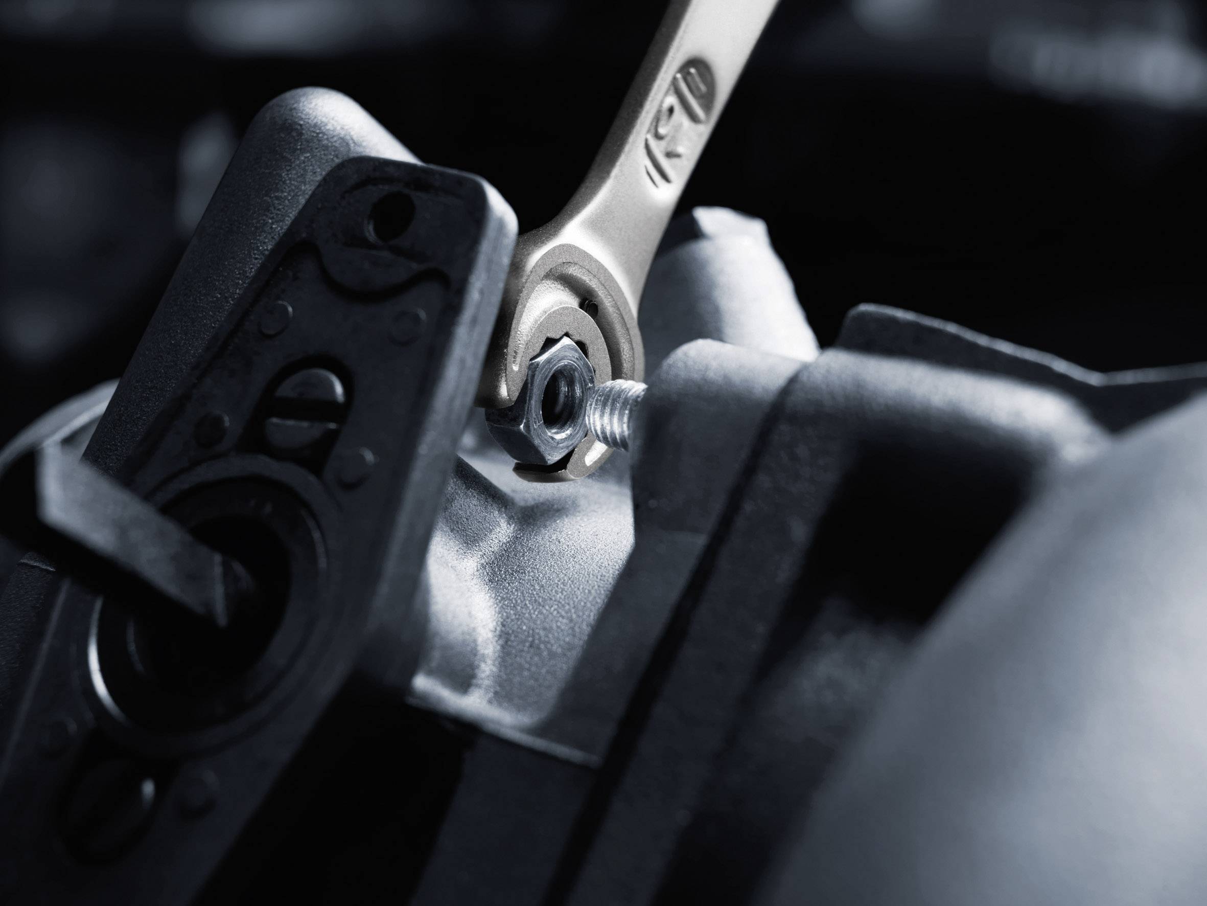 A spanner tightens a hexagonal nut on a metallic component.