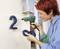 A person is attaching the house number '20' to a white wall using a glue gun.