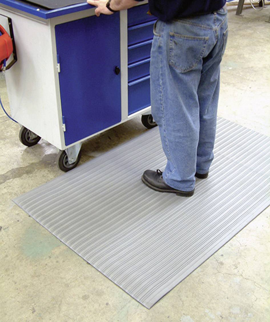 A person is standing on a grey, non-slip mat in front of a blue tool trolley. This scenario depicts a workshop environment.