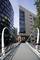 A modern pedestrian bridge passes between tall office buildings, with an old brick building in the background.