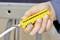 A hand is holding a yellow cable stripping tool to remove the insulation from a white cable.