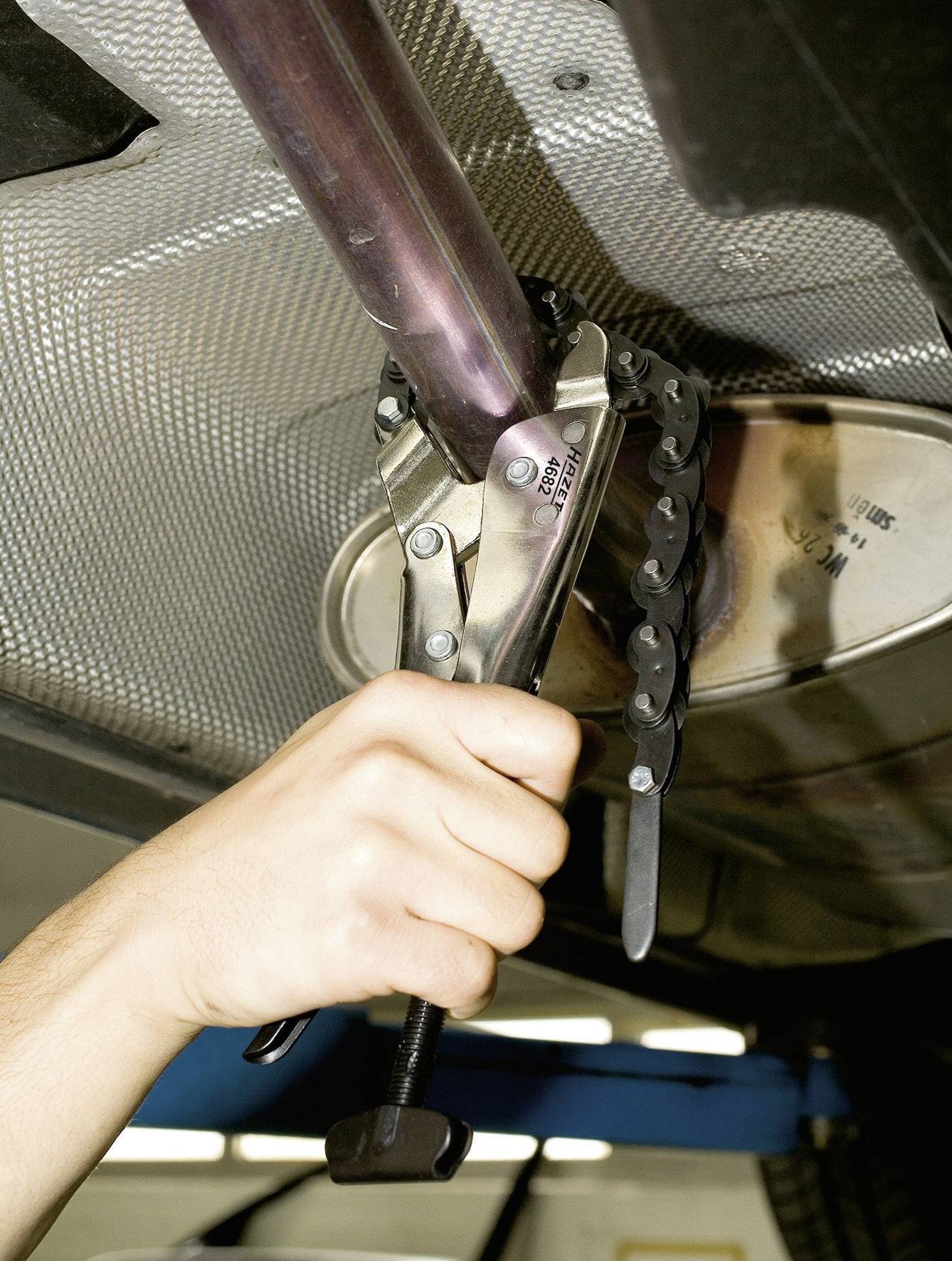 A hand is using a pipe cutter pliers to cut a metal pipe, presumably during a repair or installation.