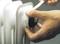 A hand turns a valve on a white radiator. Another hand holds insulation material.