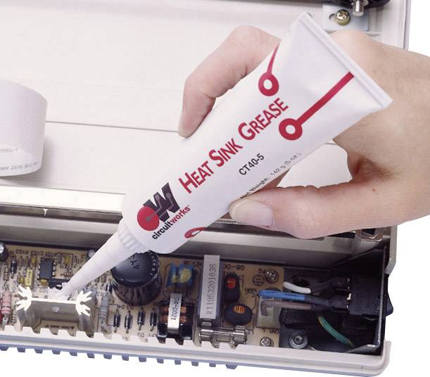 A hand is applying 'heat sink grease' to a computer chip to improve heat dissipation. The chip is mounted on a circuit board.