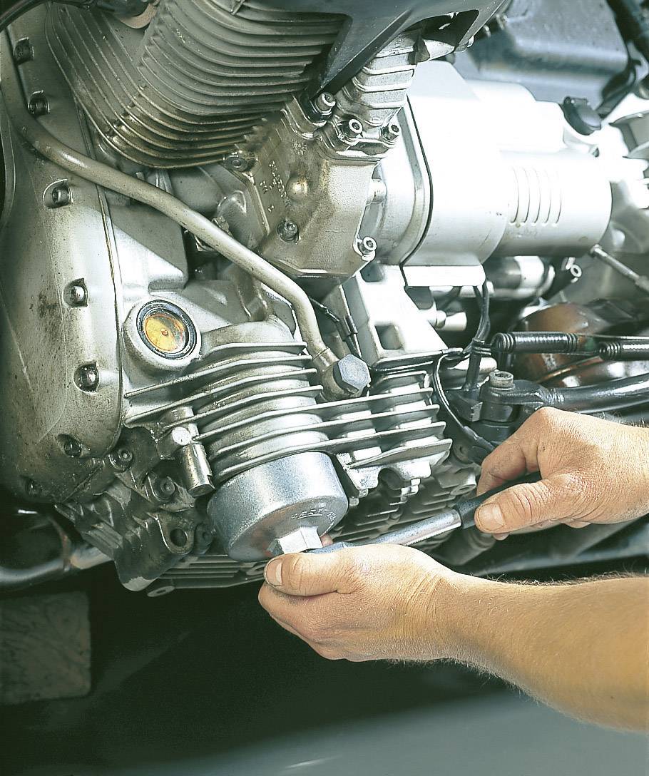 A person is servicing a vehicle's engine by tightening a screw with a tool. Mechanical parts and hands are visible.