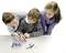 Three teenagers are looking together through a magnifying glass at laboratory containers on a table. They appear to be interested in a scientific experiment.