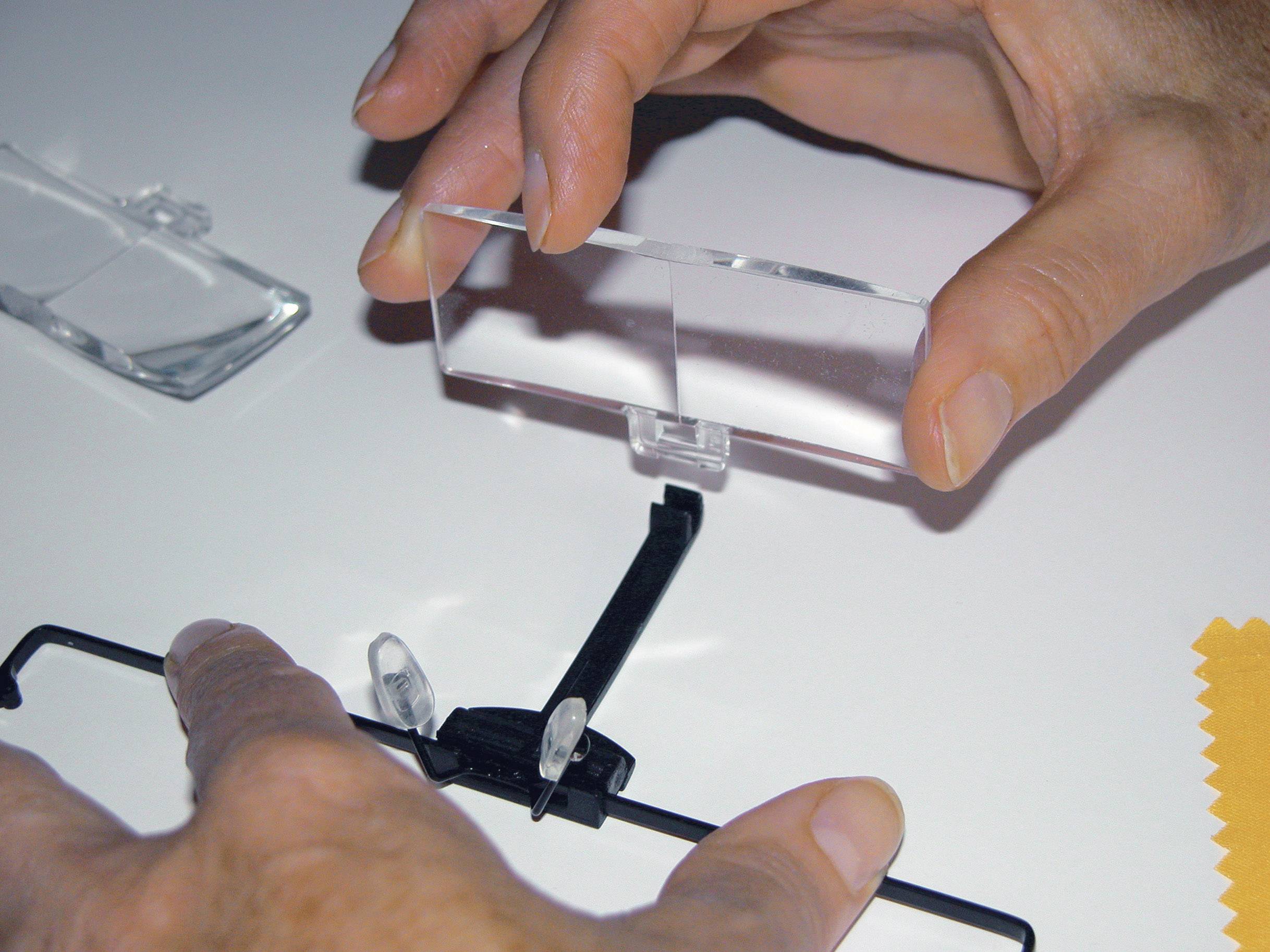 Hands are mounting a magnifying glass on a black stand against a white background.