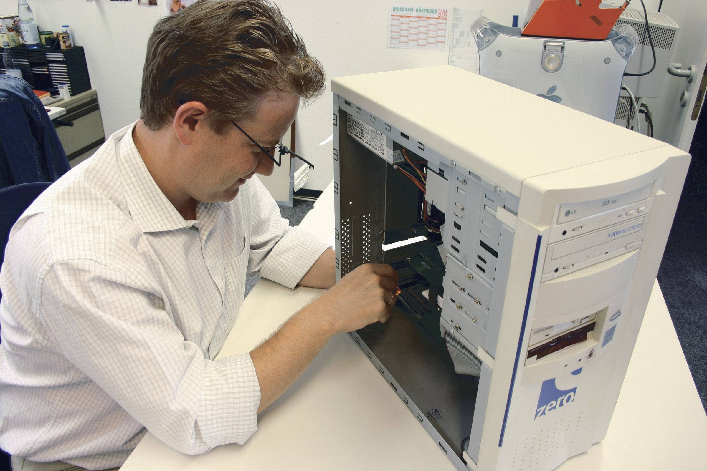A man is working on the hardware inside an open computer case in an office.