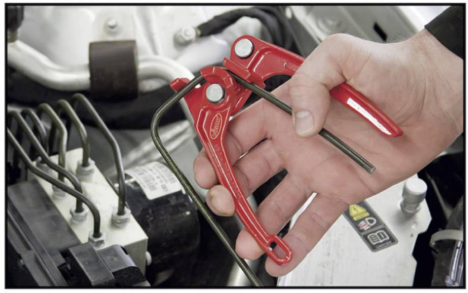 'A hand is holding a red pliers and bending a black cable in a vehicle's engine compartment.'