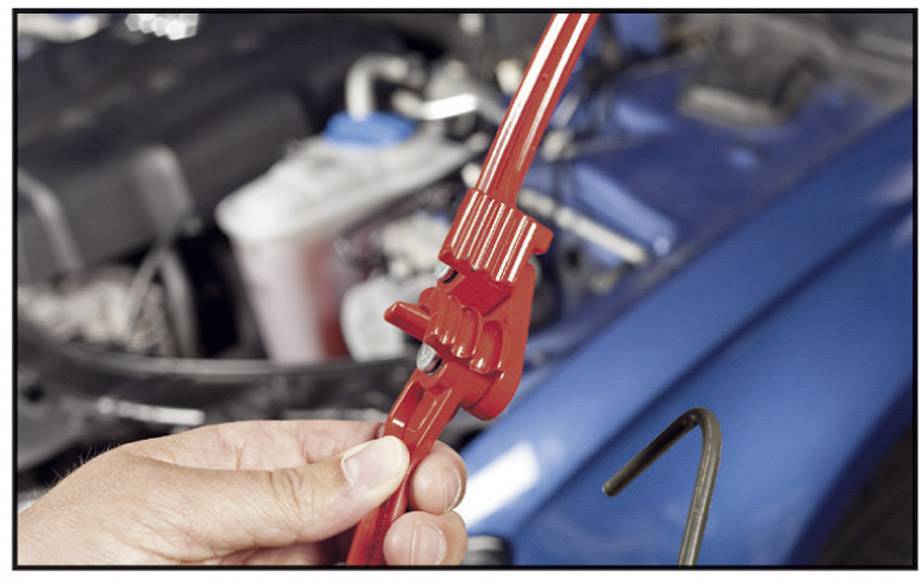 A hand holds a red adjustable spanner in front of a vehicle engine. Engine details are blurred in the background. Focus is on the tool.
