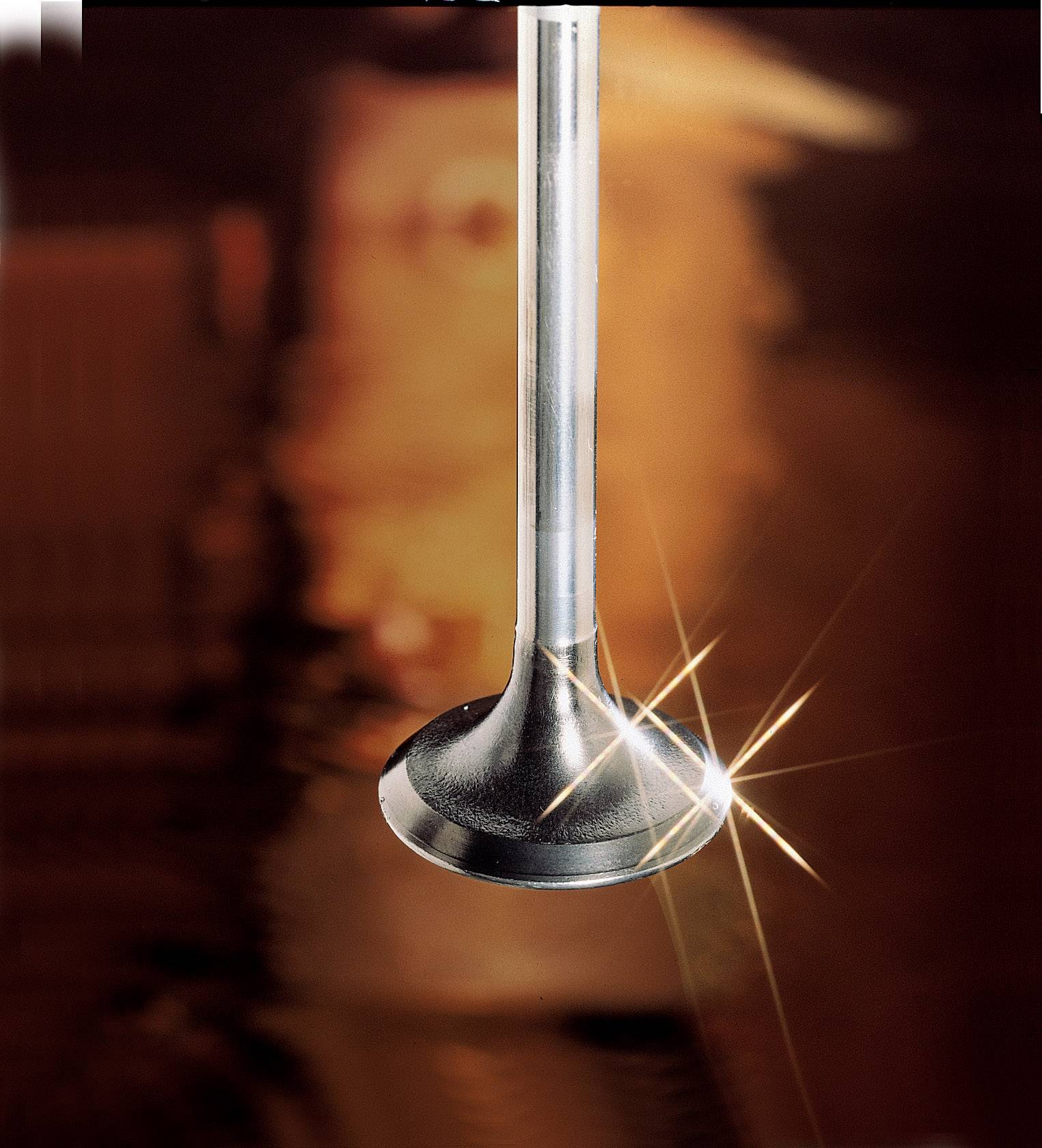 Close-up of a gleaming metal valve with light effects, against a blurred, warmly lit background.