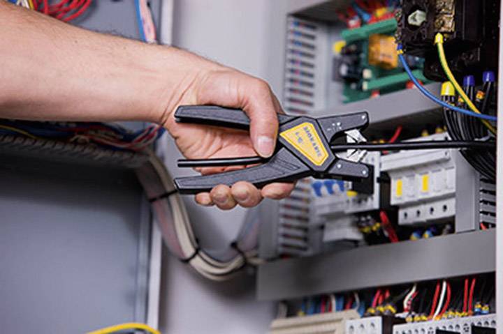 A person is using a crimping tool in an electrical distribution box to create or maintain cable connections.