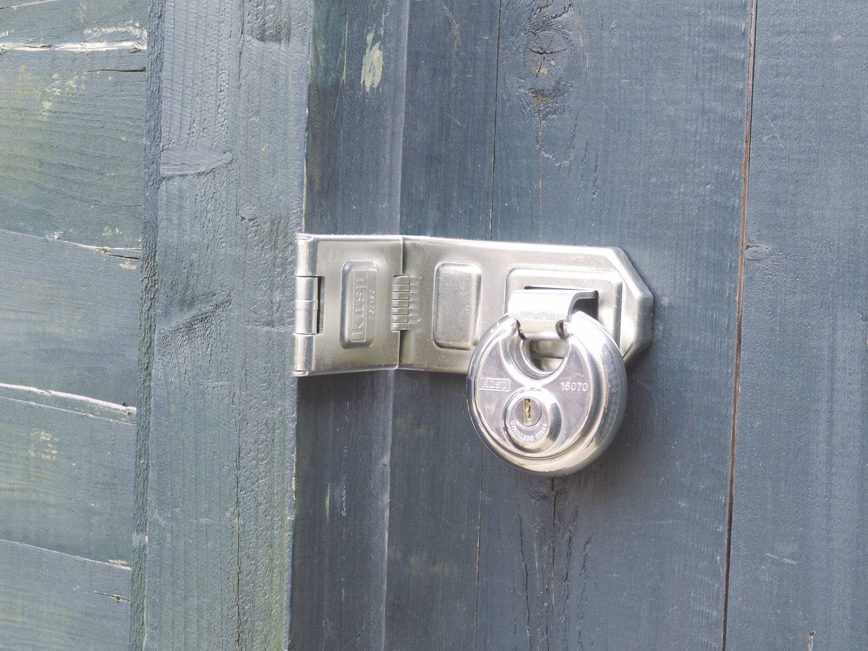 A silver padlock secures a door with a greenish, weathered wooden surface.