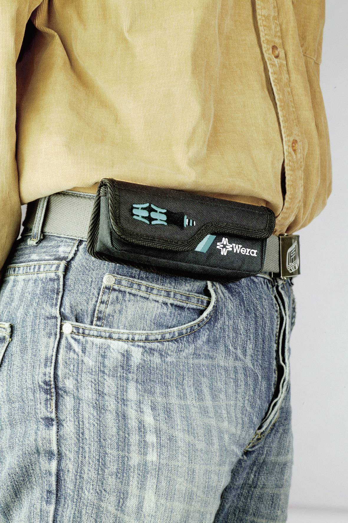 A person is wearing a black tool bag by Wera on a grey belt. The person is wearing blue jeans and a beige shirt.