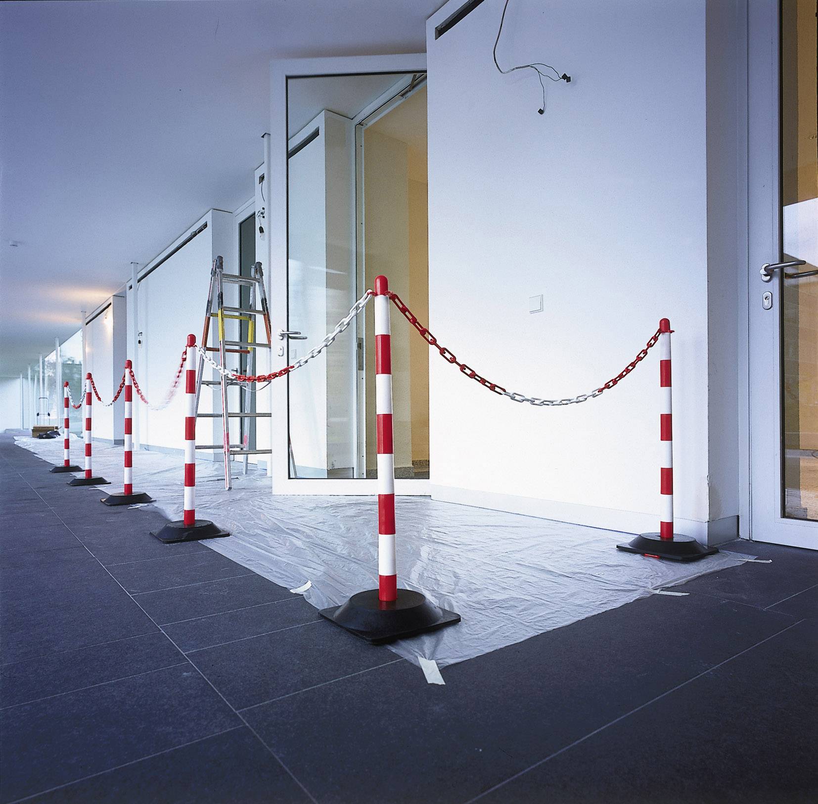Construction site barrier with red and white posts and chain in an interior area. A ladder is leaning against the wall.