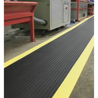 A yellow-striped safety mat is positioned in an industrial environment in front of machinery to increase slip resistance and safety.