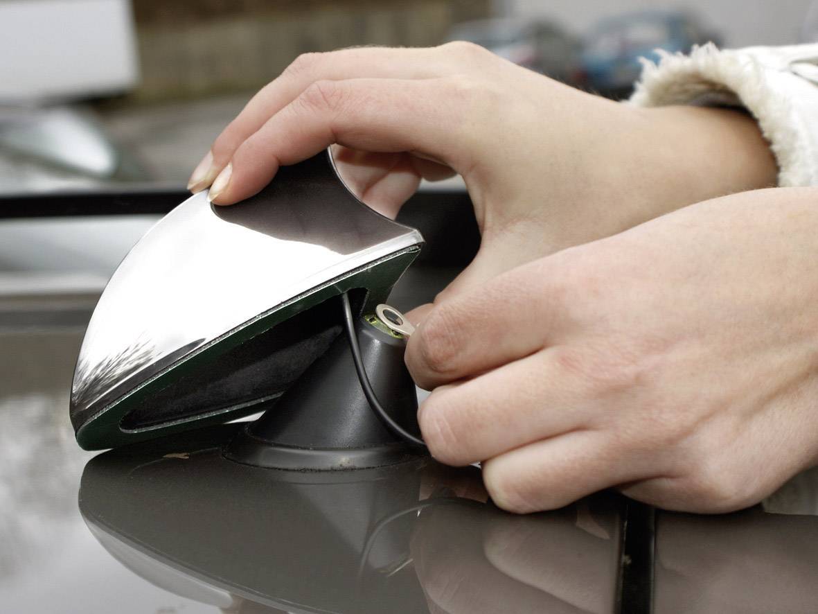 A person is mounting a silver roof aerial on a car. Hands are adjusting the aerial to establish a robust connection.