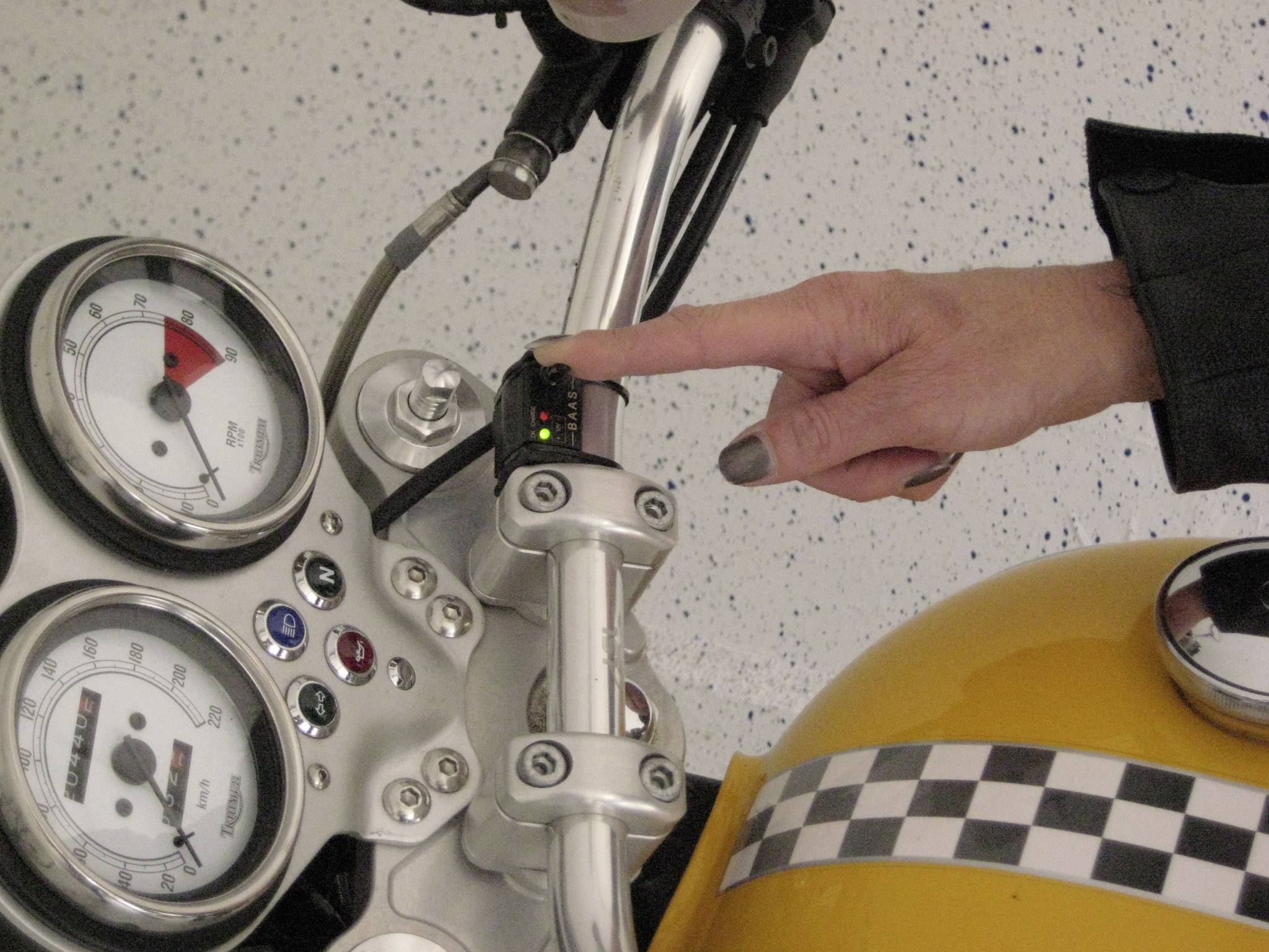 A hand presses the start button of a yellow motorbike, with the instrument panel visible.