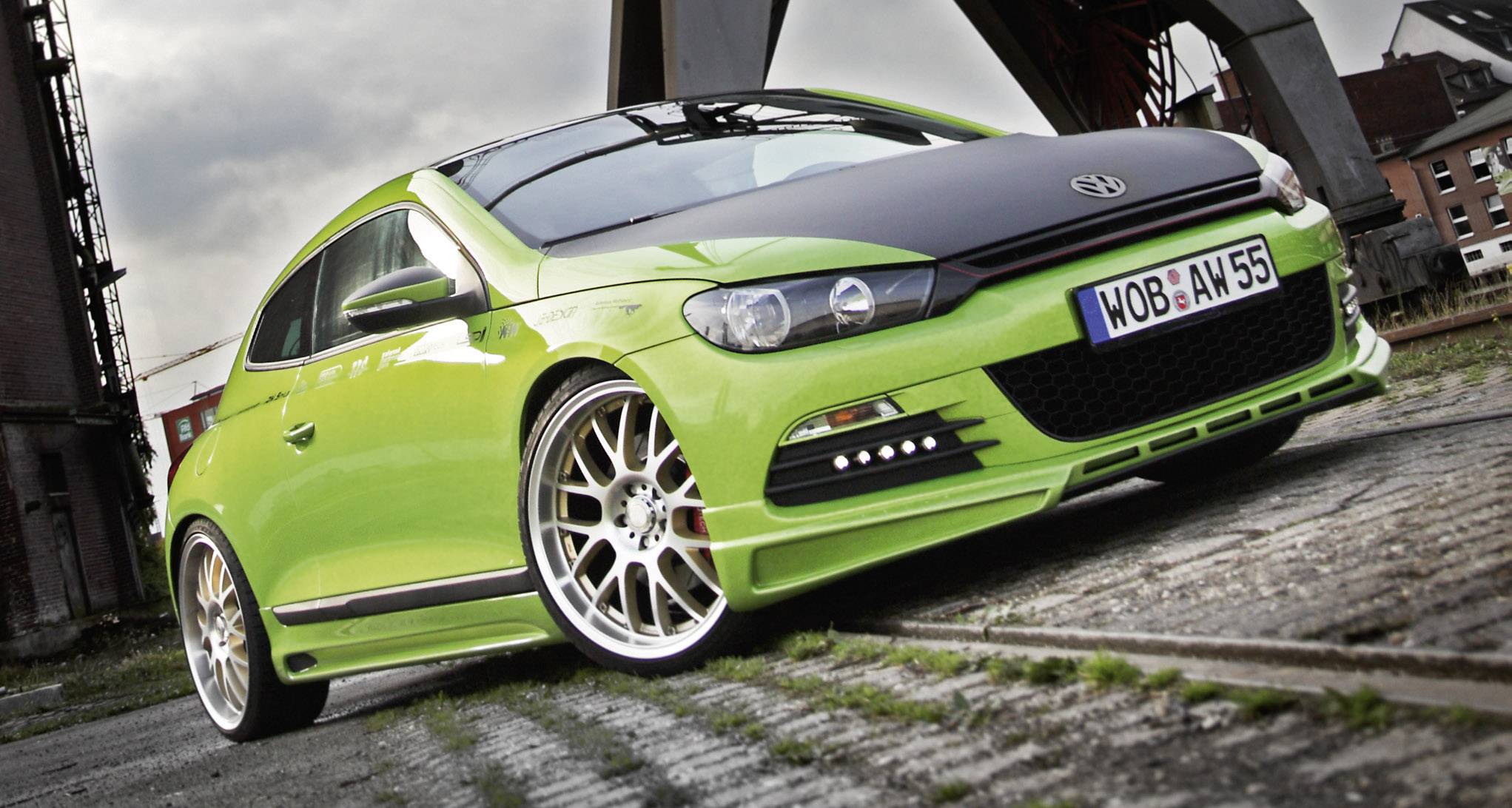A bright green sports car is parked at an angle on a paved surface in front of industrial buildings.