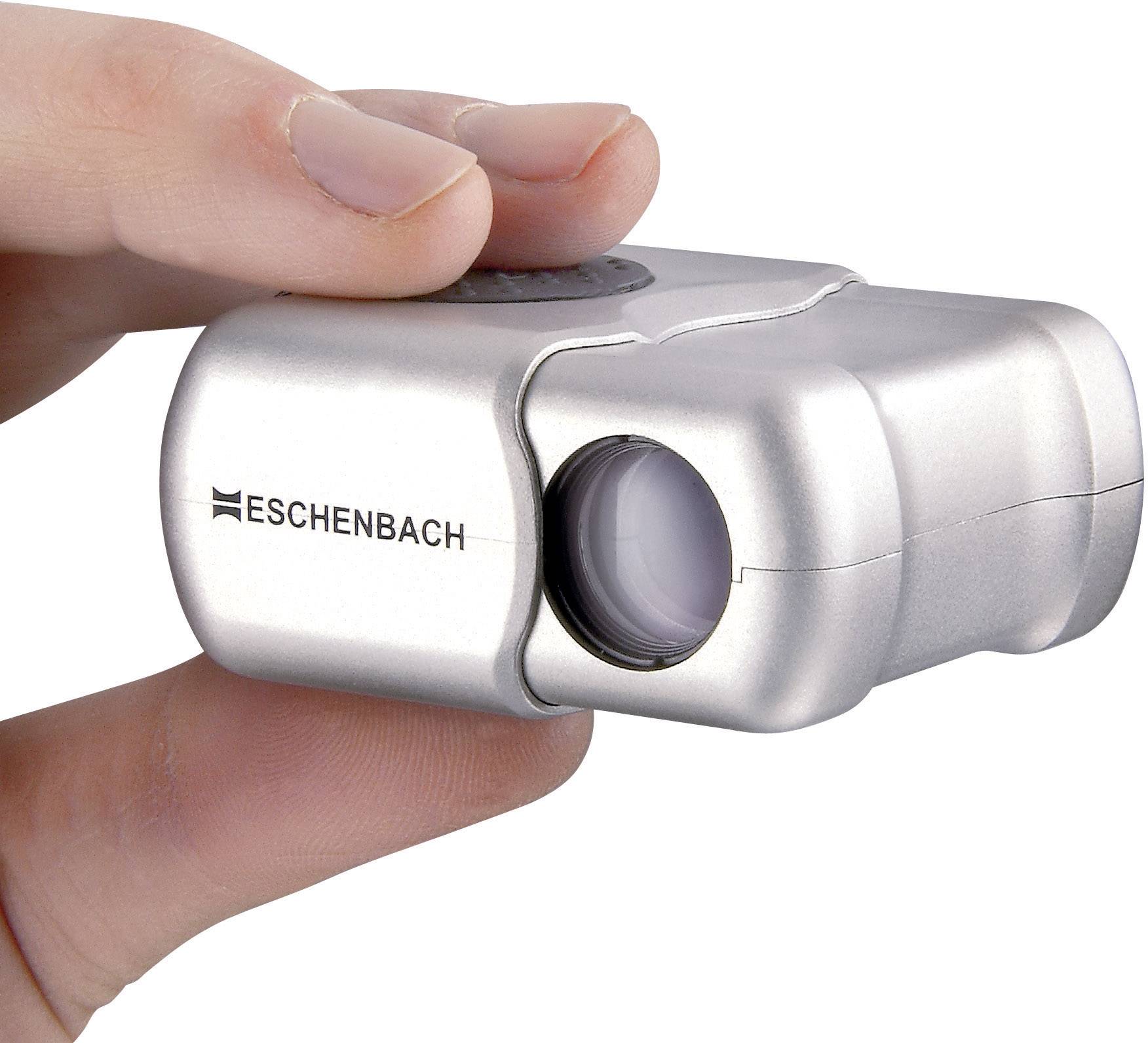 A hand is holding a silver-coloured, small device with a lens. The device is marked 'ESCHENBACH'. It appears to be an optical instrument.