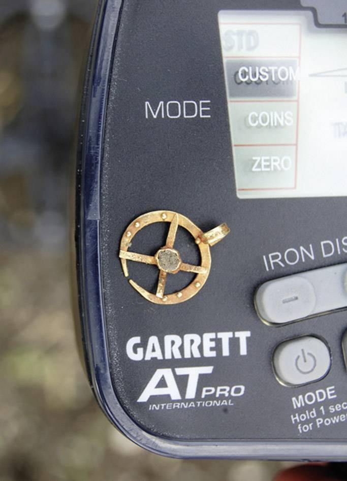 A metal object in the shape of a wheel lies on a metal detector screen, displaying various operating modes.