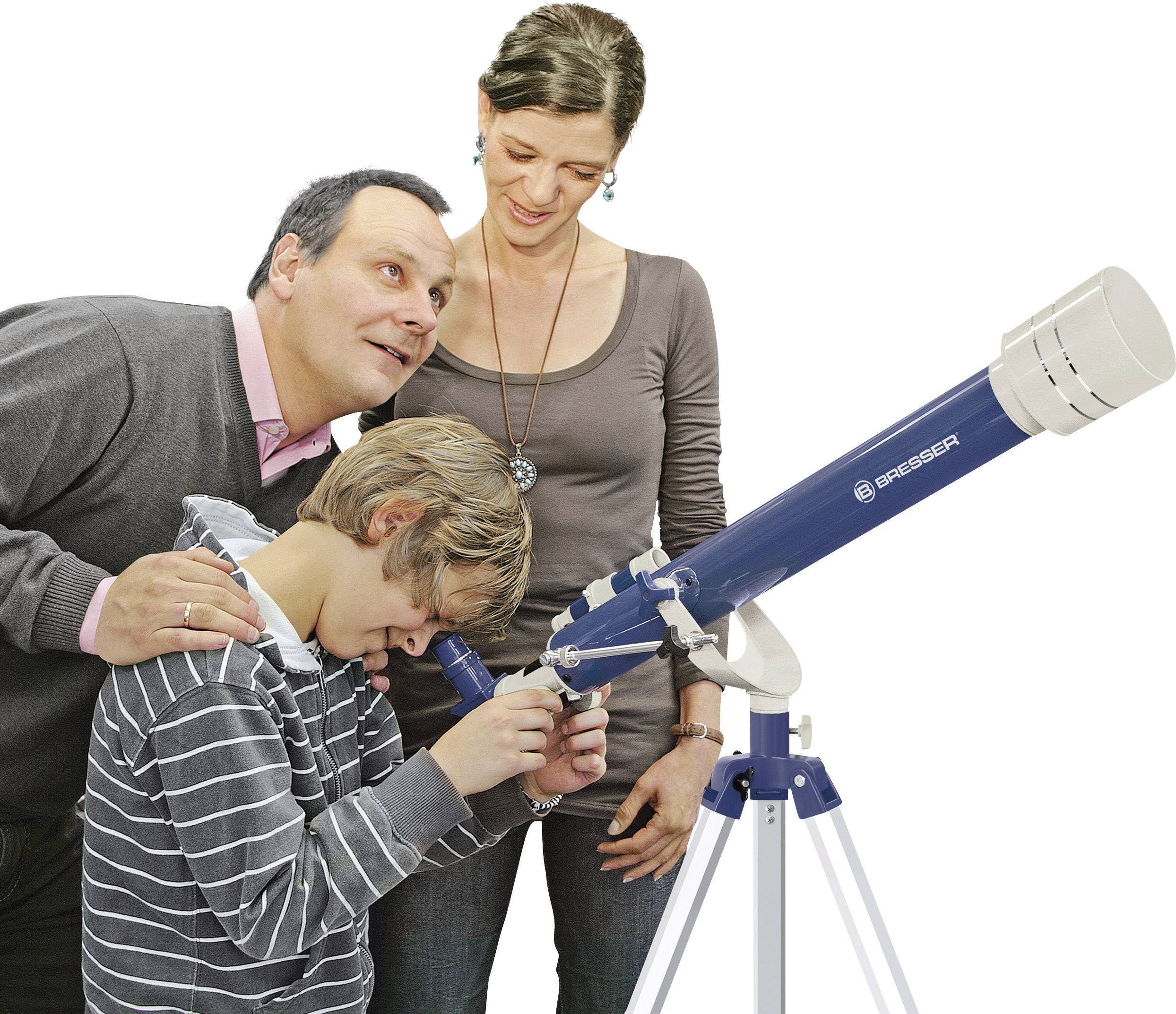 A boy looks through a telescope while a man and a woman stand beside him and smile. They are observing the sky together.