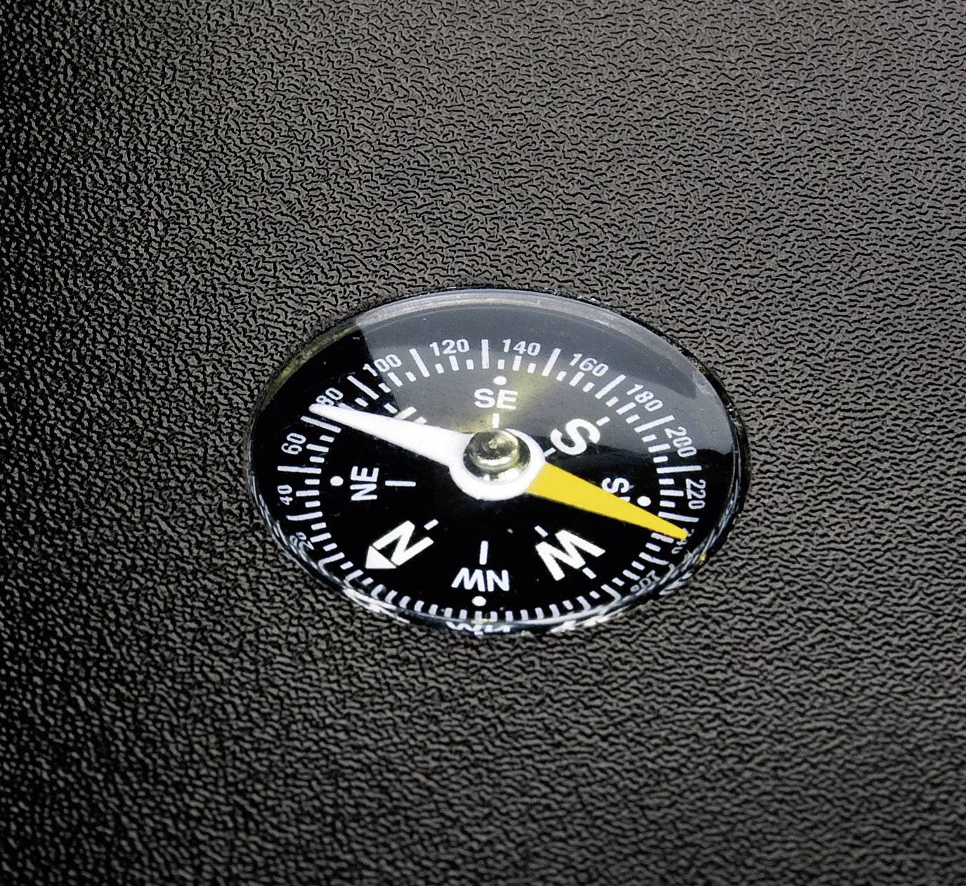 A compass indicates the cardinal directions, lying on a structured, black surface. The needle points south.