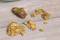 Gold nuggets lie on a wooden table. They vary in shape and size, shine brightly and display irregular surfaces.