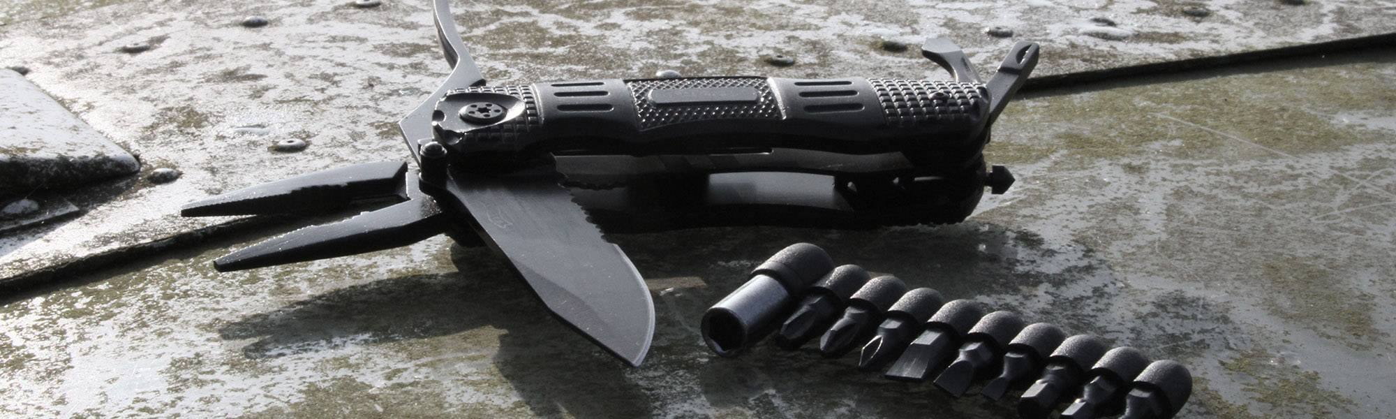 Multifunctional tool with unfolded blades and bit set lying on a textured metal surface.