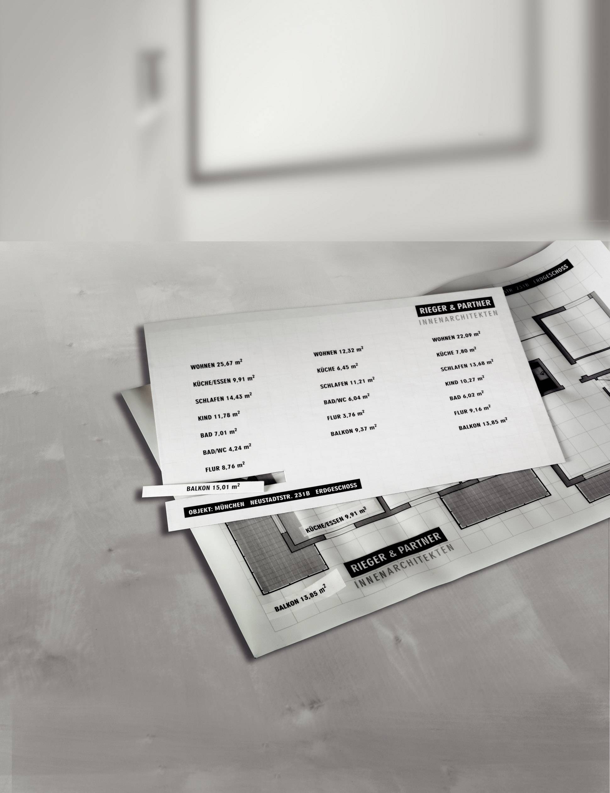 Black and white architectural plans and price lists on a table. The plans show floor layouts and the lists contain dimensions and prices.