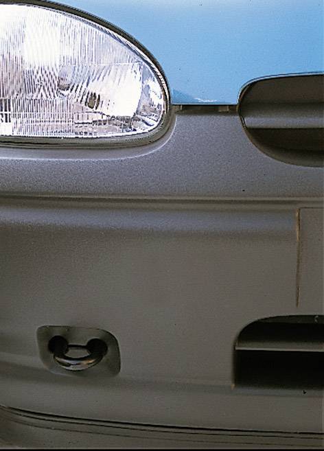 A silver car bumper shows a headlight and a towing eye at the bottom left, against a blue background.