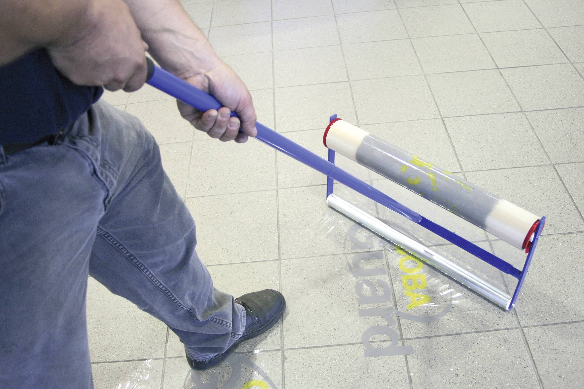 A person is using a blue paint roller to print yellow letters on grey tiles.