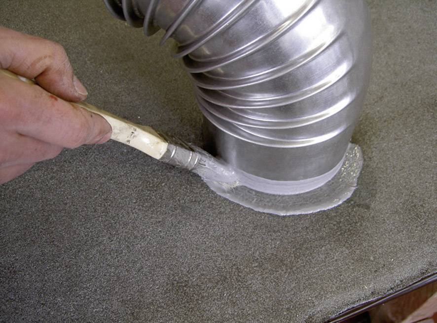 A hand applies white sealant with a brush to a metal tube on a grey surface.