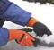 A person wearing orange gloves is shovelling snow with a small shovel. A blue item of clothing is visible.