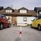 Car park with a red and white barrier between two parked cars in front of a residential house with dormer windows.