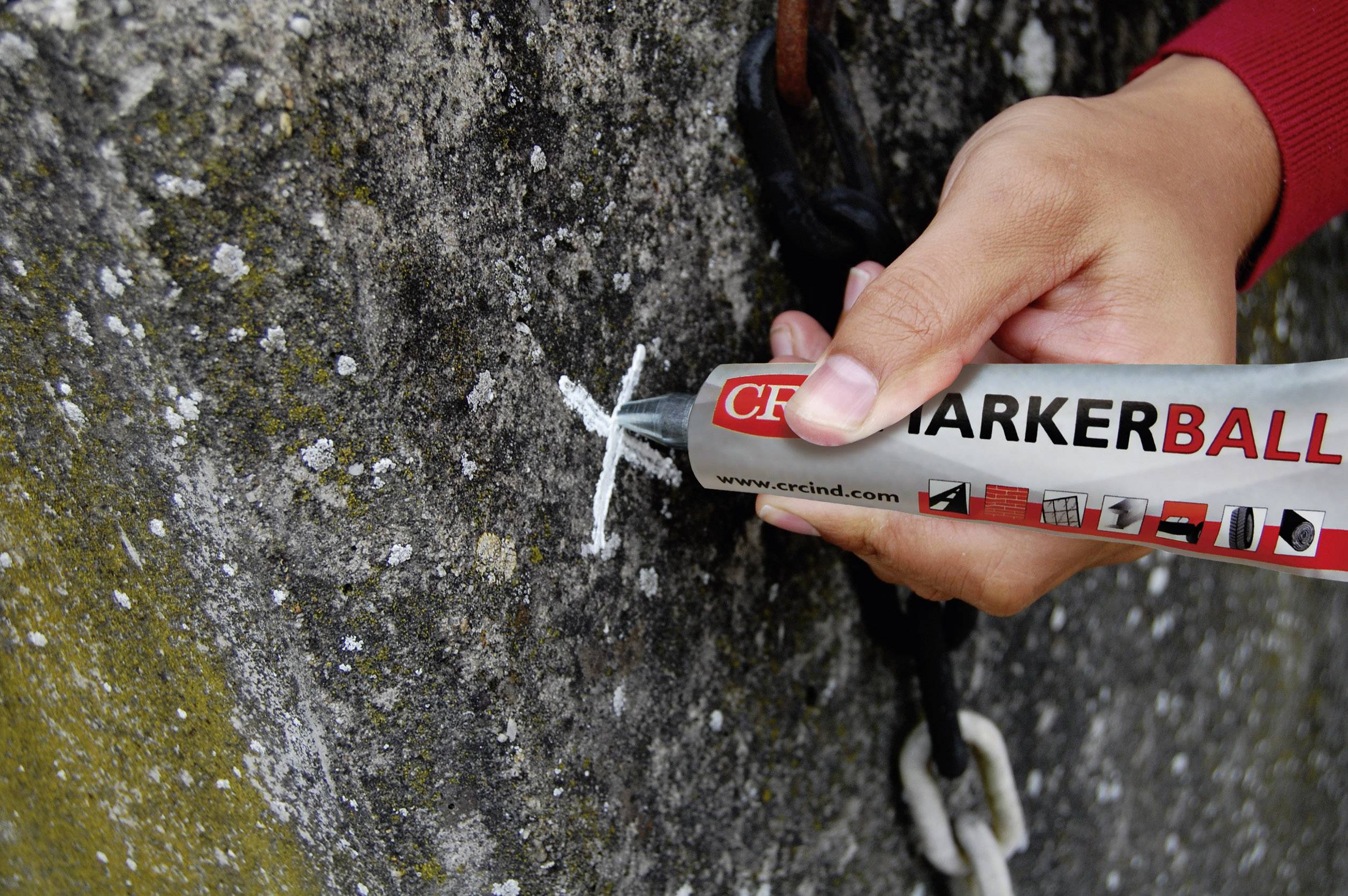 A hand holds a red marker and draws a cross on a rough stone surface, next to a chain.