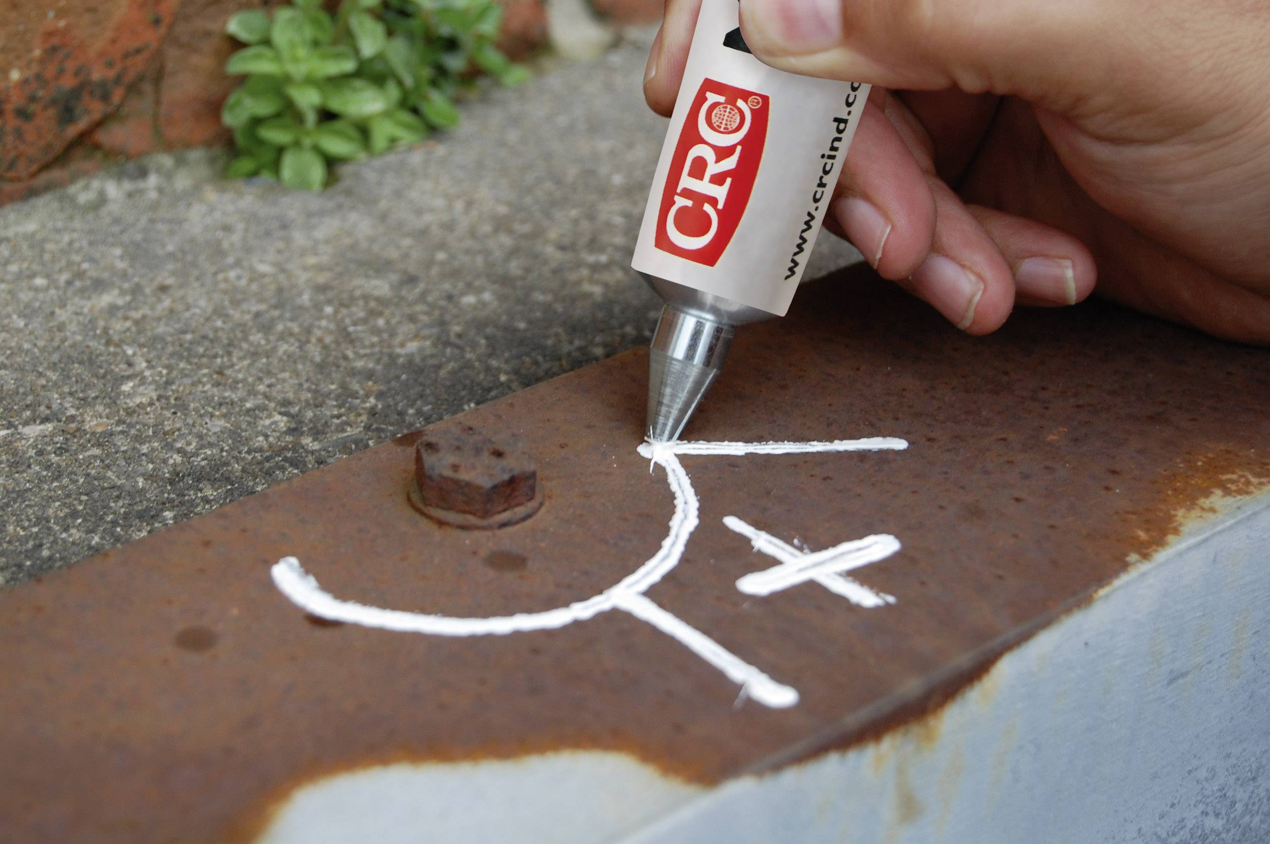 'CRC' adhesive is applied to a metal surface in the shape of a smiling face. Plants can be seen in the background.