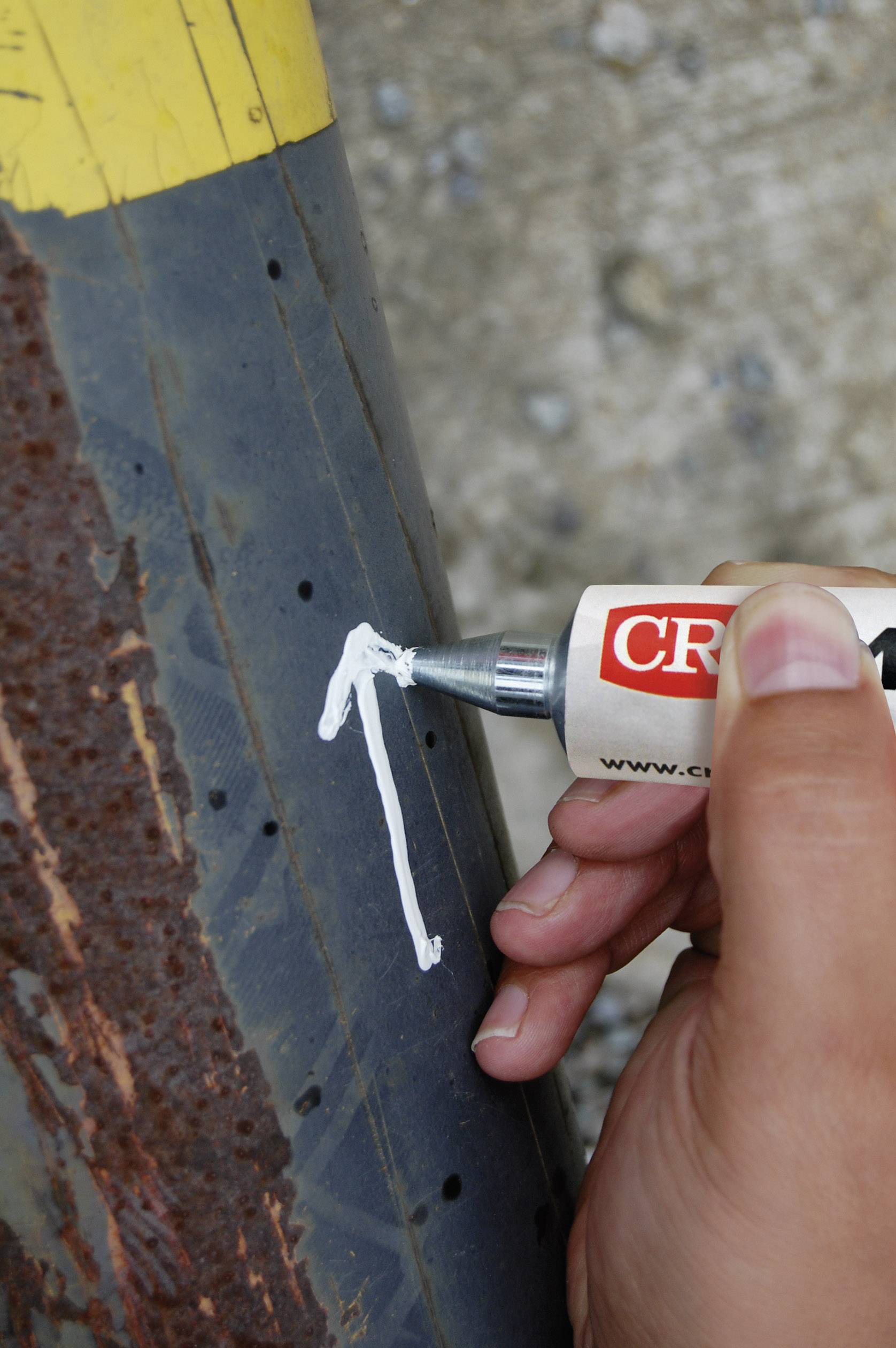 A person is writing with a white marker on a rusty, black pipe. The environment appears industrial and slightly weathered.