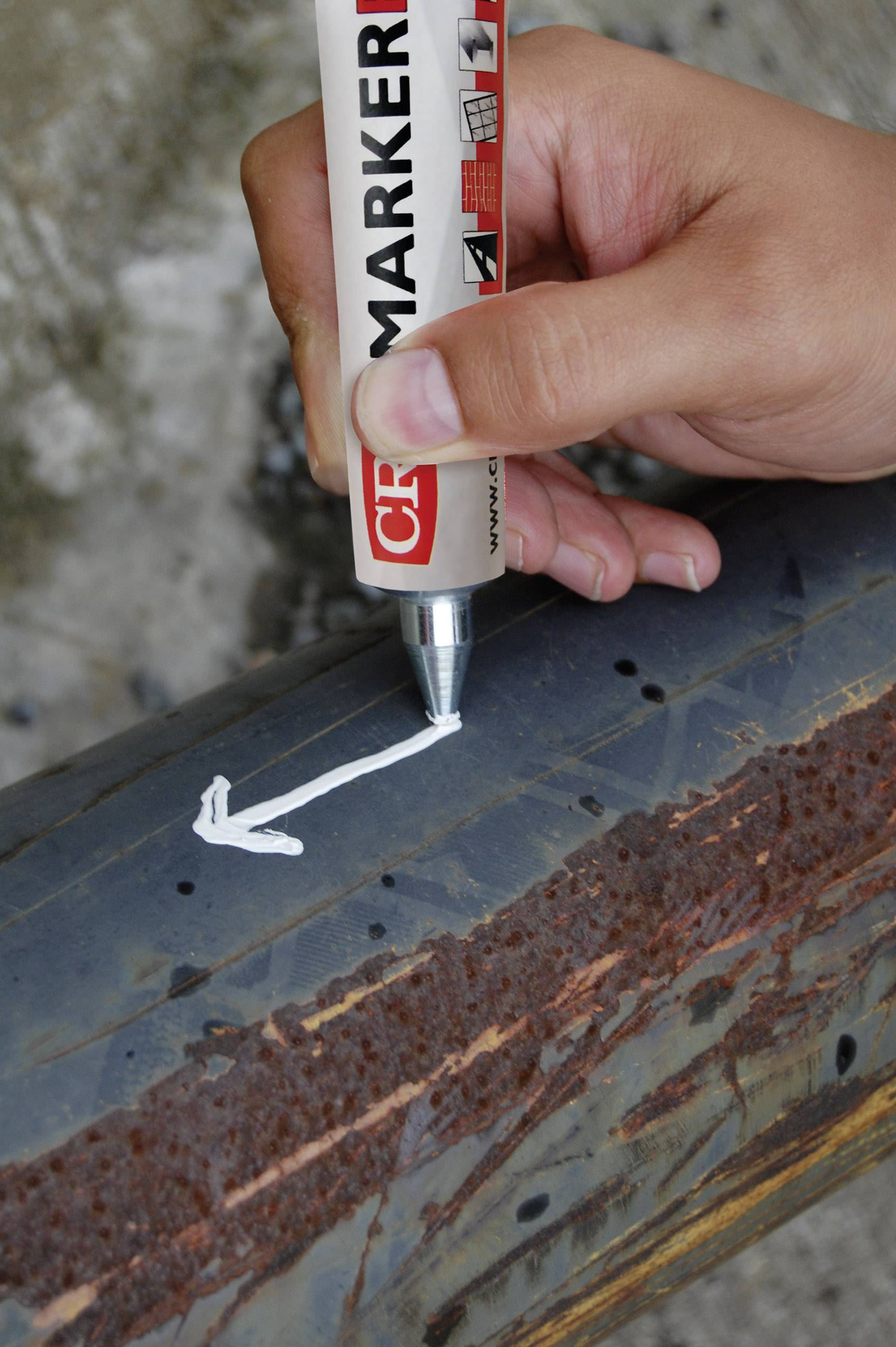 A hand draws an arrow with a white marker on a rusty pipe.