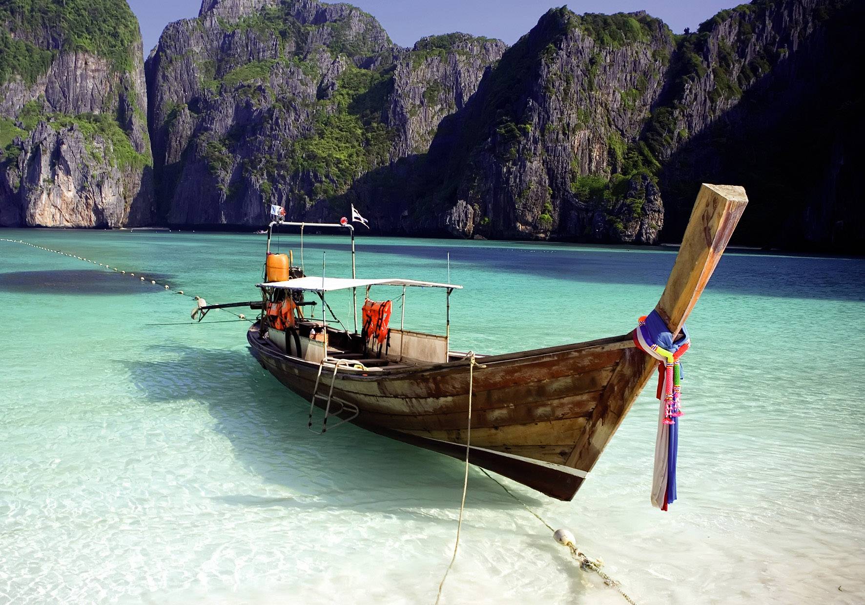 A traditional wooden boat rests in clear turquoise water before a rocky, verdant coastal landscape.