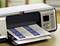 A printer on a table is outputting a sheet of labels. The display and control buttons are visible.