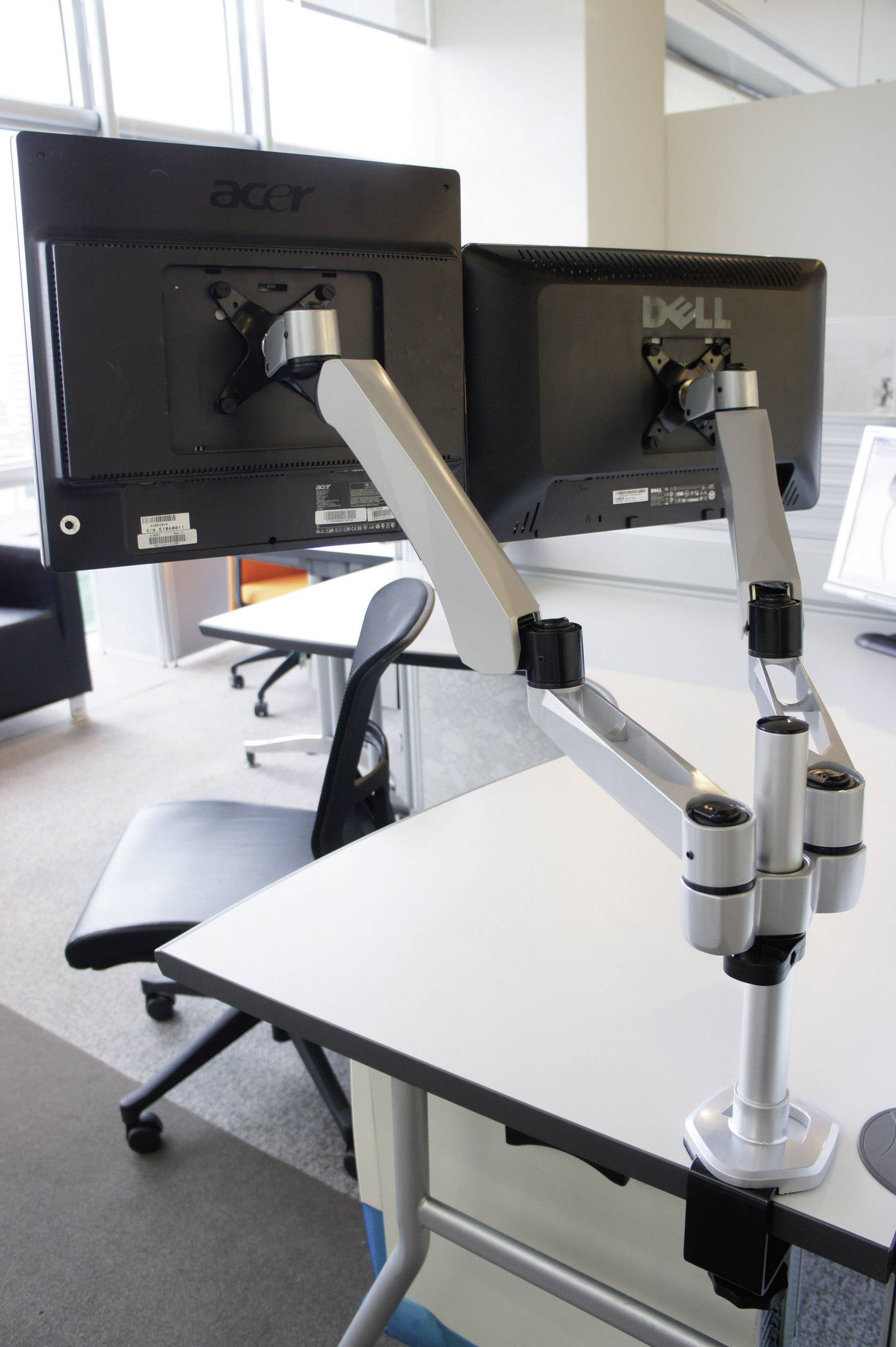 A modern workspace with two monitors mounted on sleek, adjustable stands on a white desk in an office.