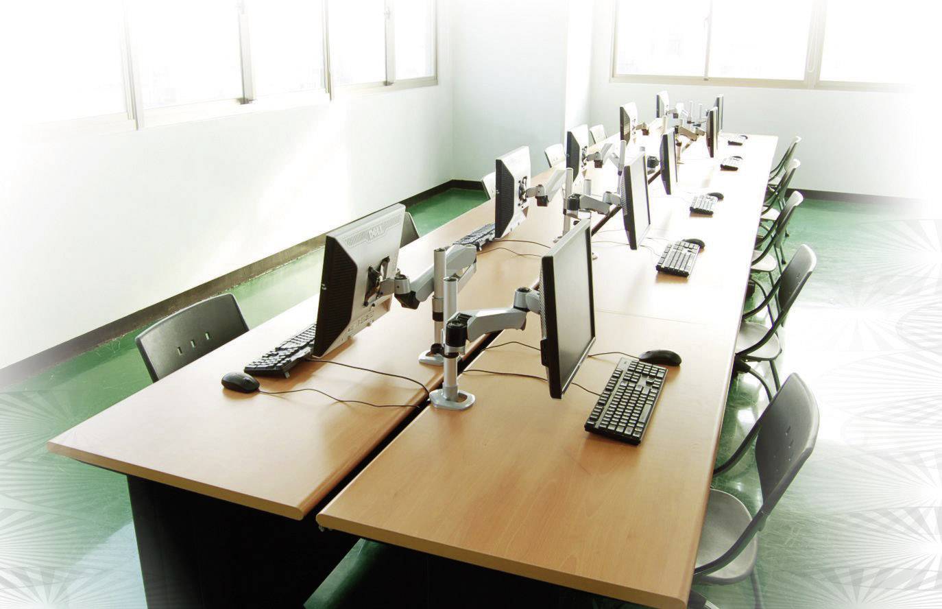 Row of computers on a table in a bright room. All screens, keyboards, and mice are evenly arranged.