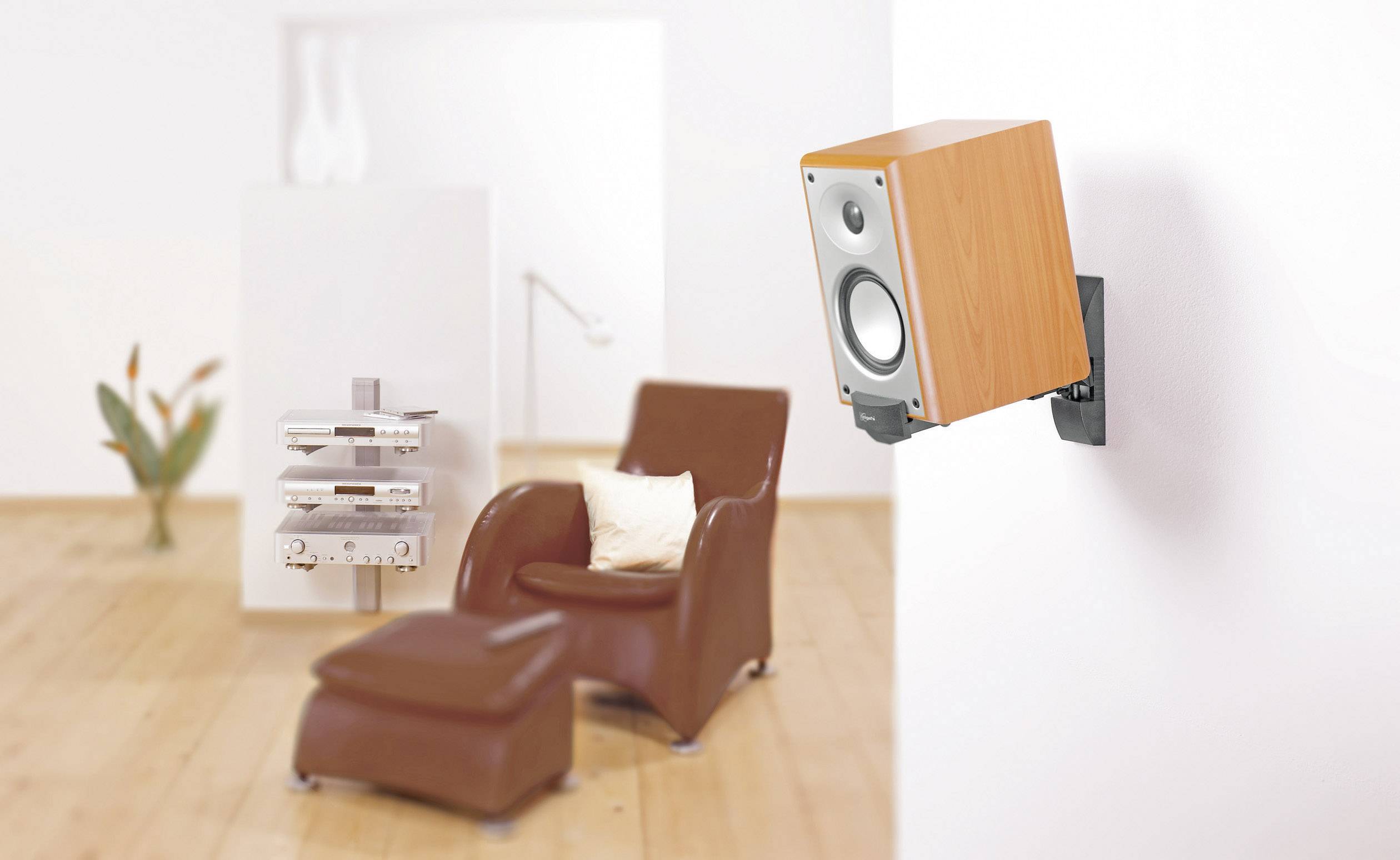 Speakers mounted on the wall in a modern living room with a brown armchair and plants in the background.
