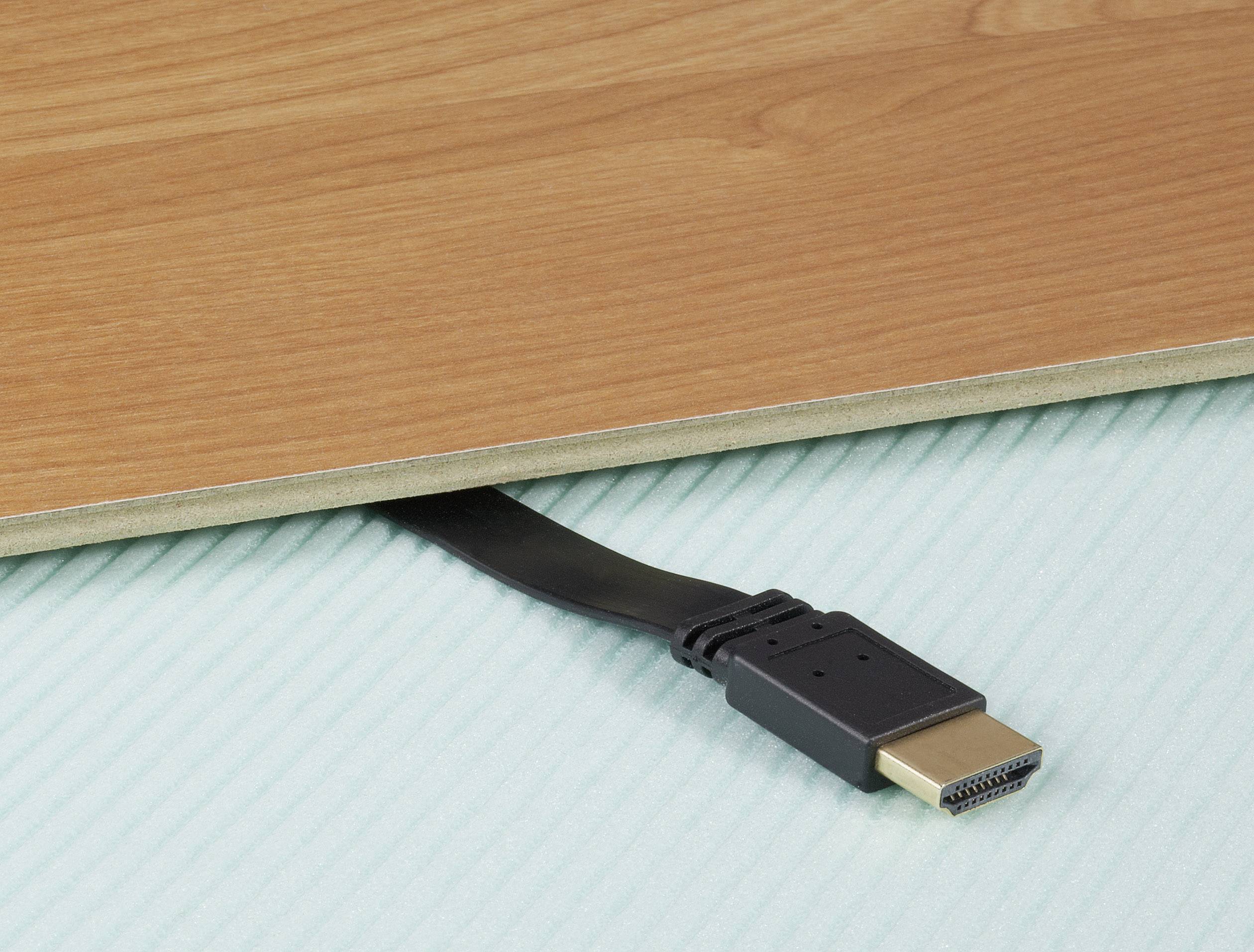 A flat HDMI cable is pulled out from underneath a wooden board against a pastel-coloured background to demonstrate its flexibility.