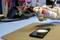 Une personne pulvérise un produit de nettoyage sur un smartphone posé sur une table. Des outils sont visibles en arrière-plan.