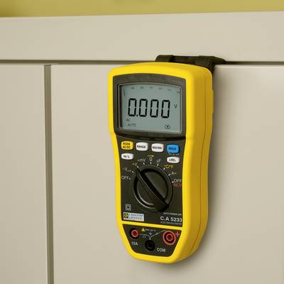 Un multimètre numérique jaune est suspendu à une armoire blanche. L'affichage indique '0,000 V'. Différentes fonctions de mesure sont sélectionnables.