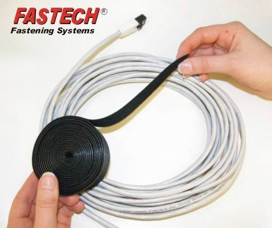 Deux mains regroupent un épais câble gris avec une bande auto-agrippante noire. En haut à gauche est inscrit 'FASTECH Fastening Systems'.