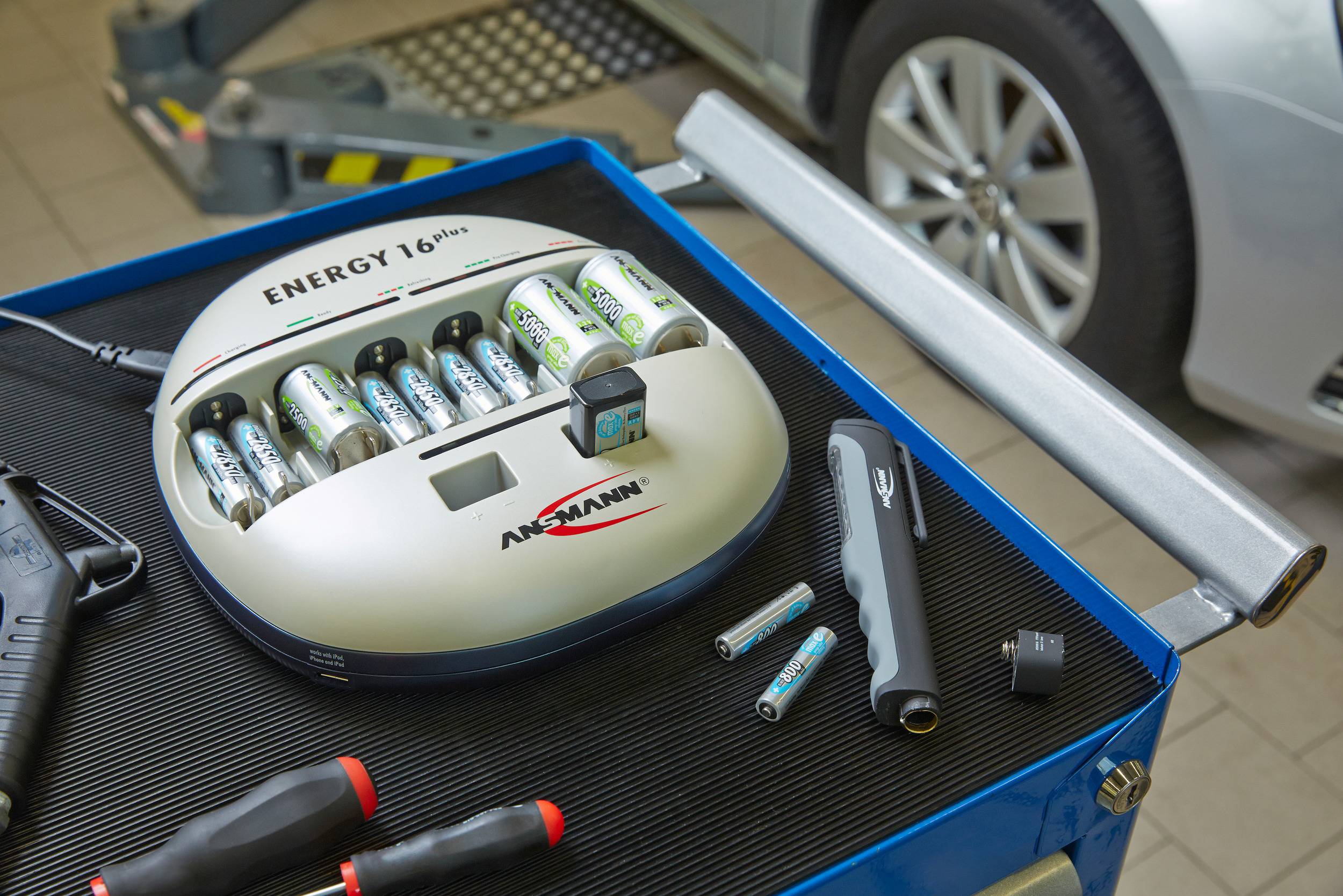 Chargeur de batterie sur l'établi avec des batteries chargées, des outils à côté. Voiture en arrière-plan. Environnement d'atelier.